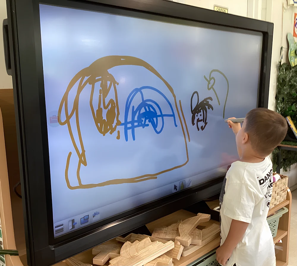 Child drawing on an interactive whiteboard in a preschool classroom.