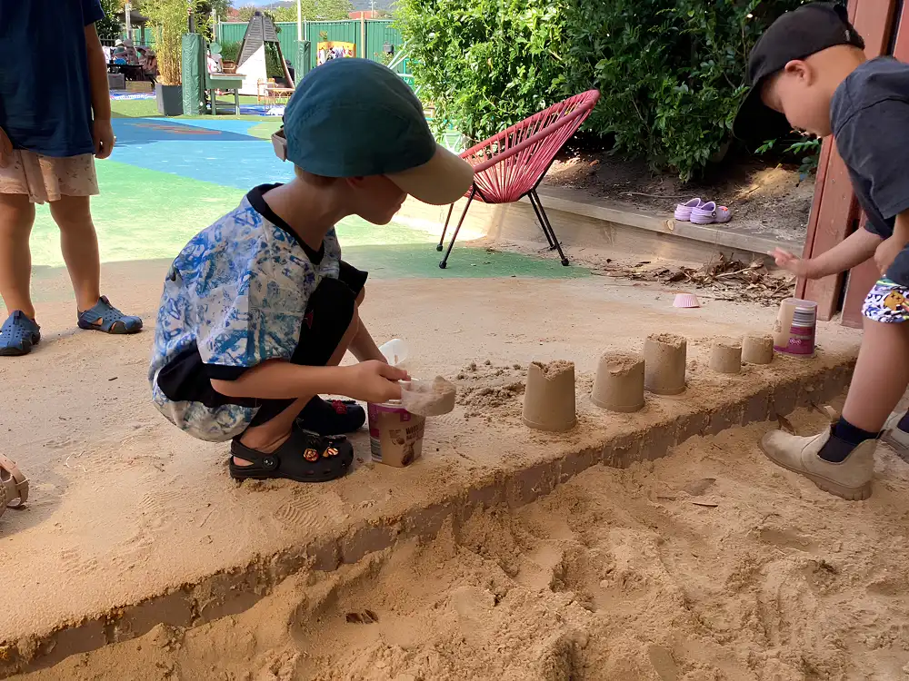 Children playing in a sandpit building sandcastles using small buckets and scoops outdoors at children's centre Woonona