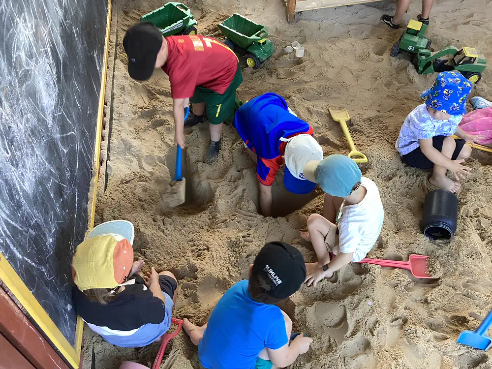 Children digging in a sandpit using shovels and buckets during outdoor play